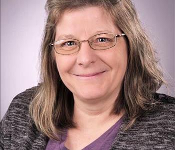 Female with medium length brown hair and glasses. She is wearing a purple shirt.